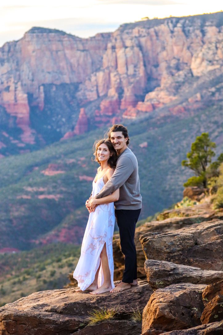 A romantic scene unfolds on a rocky ledge with majestic red rock formations in the distance in Sedona Arizona.