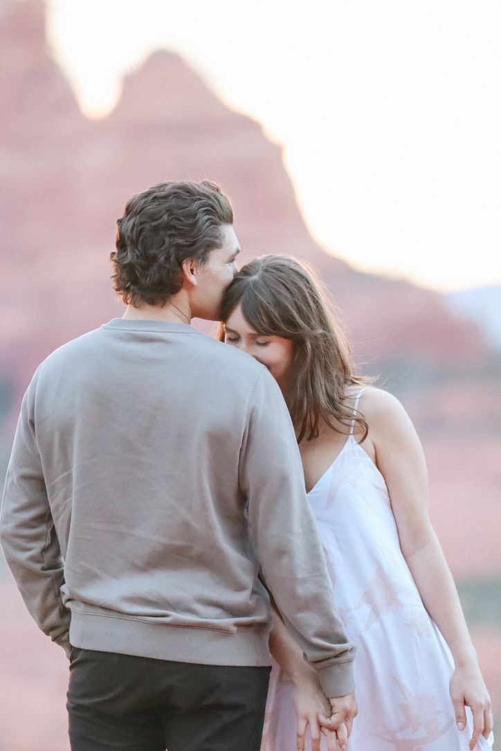 A romantic couple embraces against a backdrop of red rock formations at sunset in Sedona Arizona.