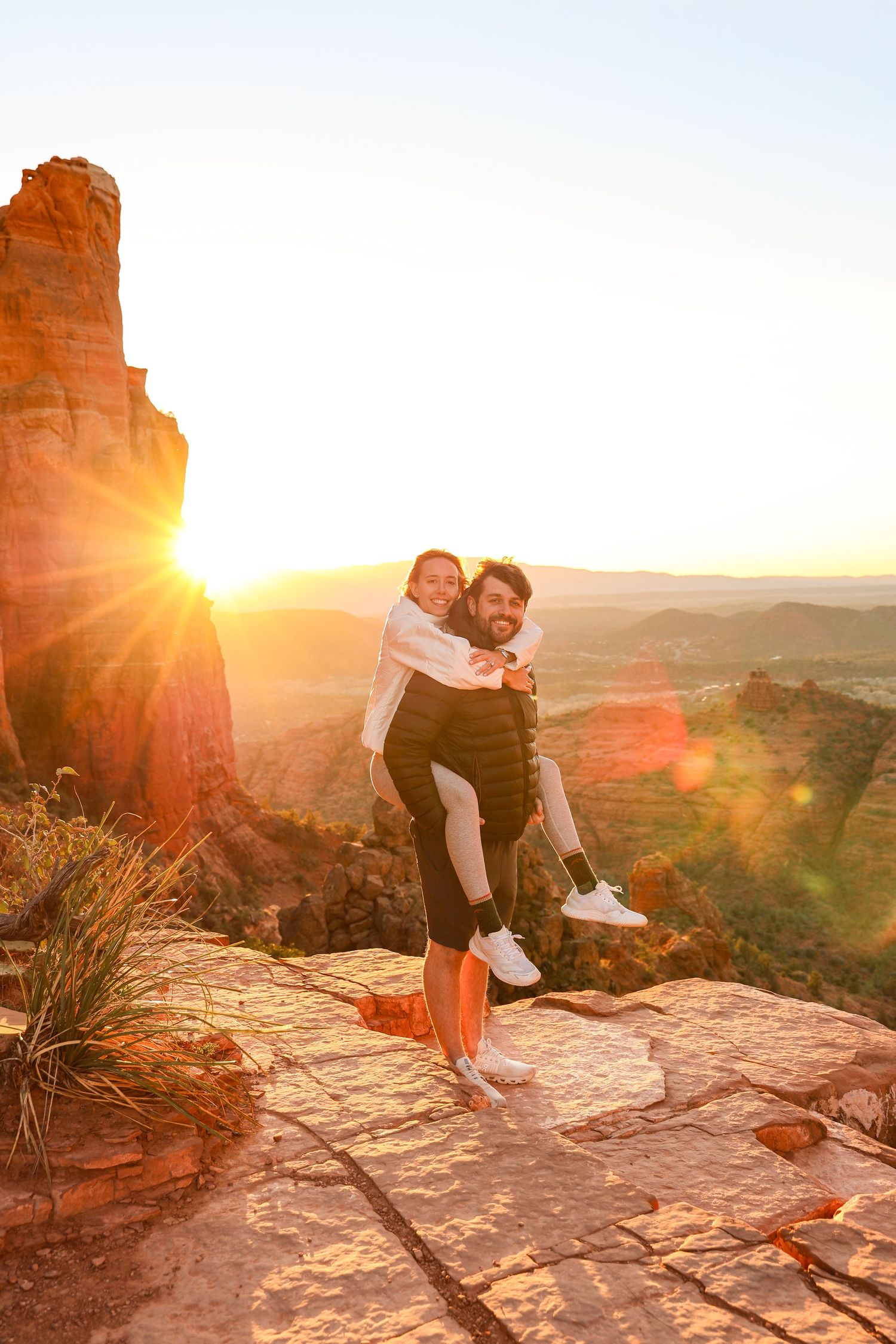 A couple embraces during golden hour on a scenic red rock overlook with dramatic sunset lighting in Sedona Arizona at Cathedral Rock.