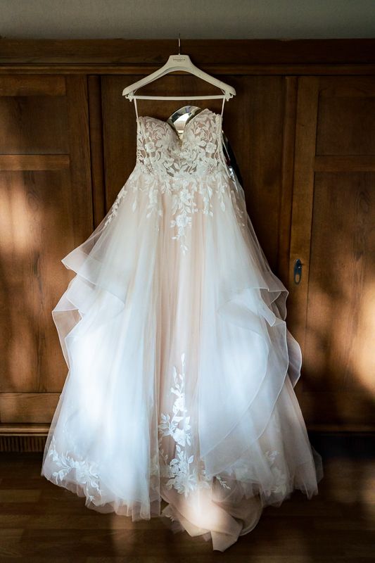 Elegant strapless A-line wedding dress with lace appliques and tulle skirt hanging on wooden wardrobe.