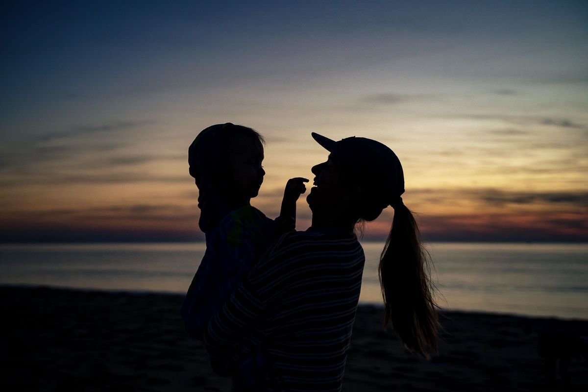 Silhouette of mother holding child against vibrant ocean sunset sky on beach.