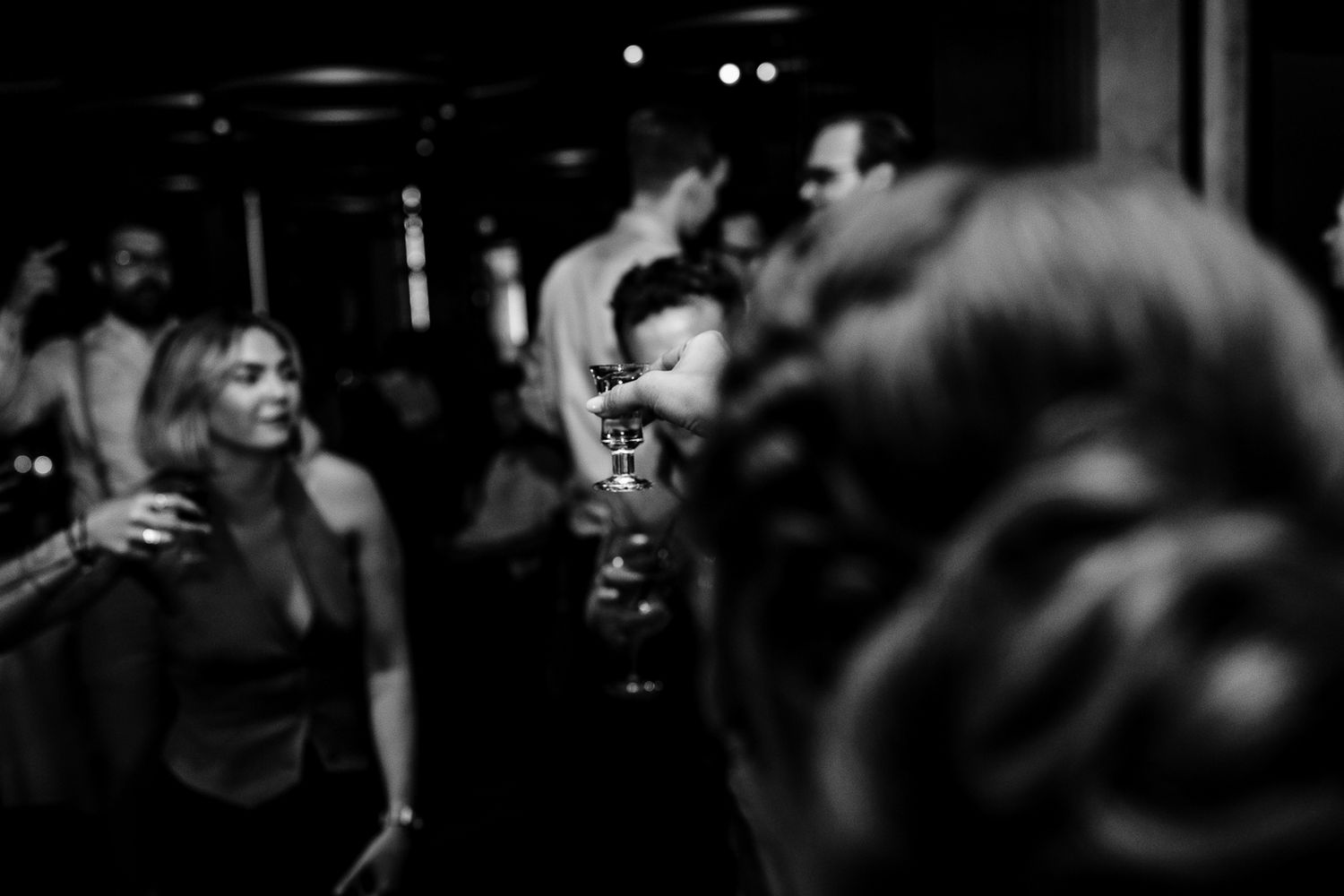 Black and white photo of people socializing and dancing at a dimly lit party or nightclub event.