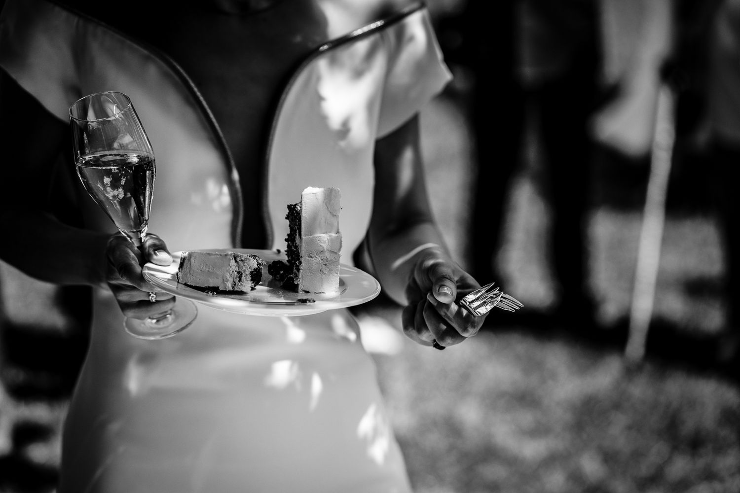 Black and white photo of hands holding a plate with cake and champagne glass at a wedding reception.
