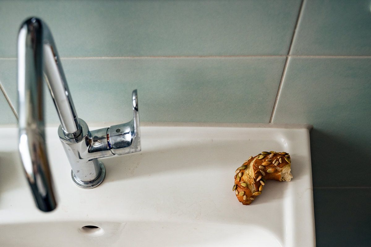 Chrome bathroom faucet on white sink with green tiles and a crumpled golden wrapper on the edge.