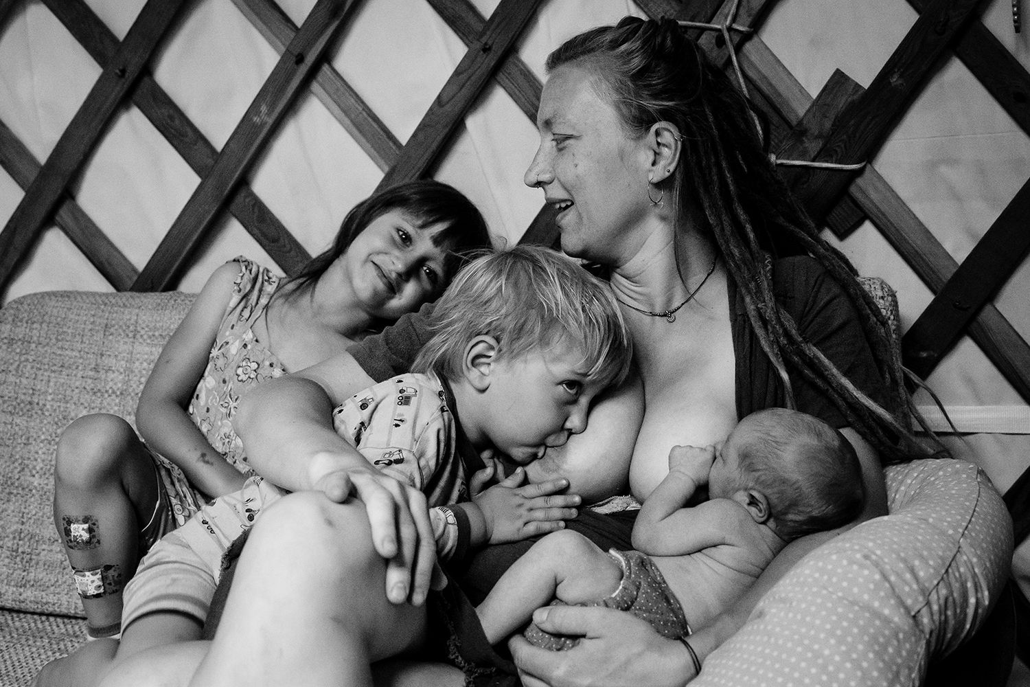 Familienfoto von einer Mutter, aus Siegen, die zwei Kinder stillt und ein drittes liebevoll in ihrem Arm hält.