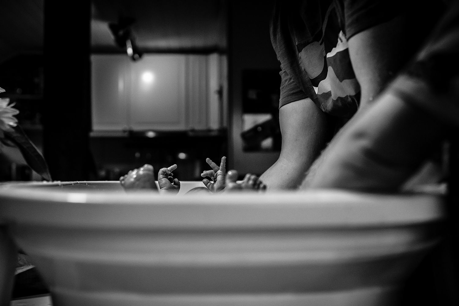 Black and white photo of person kneading dough in a white bowl in a dimly lit kitchen.