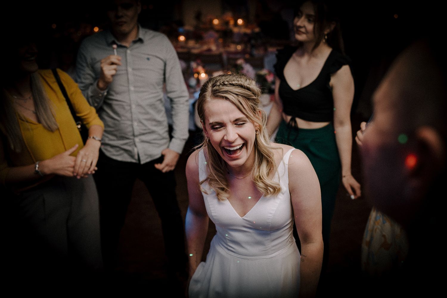 Bride laughing joyfully on the dance floor surrounded by guests at a lively wedding reception celebration.