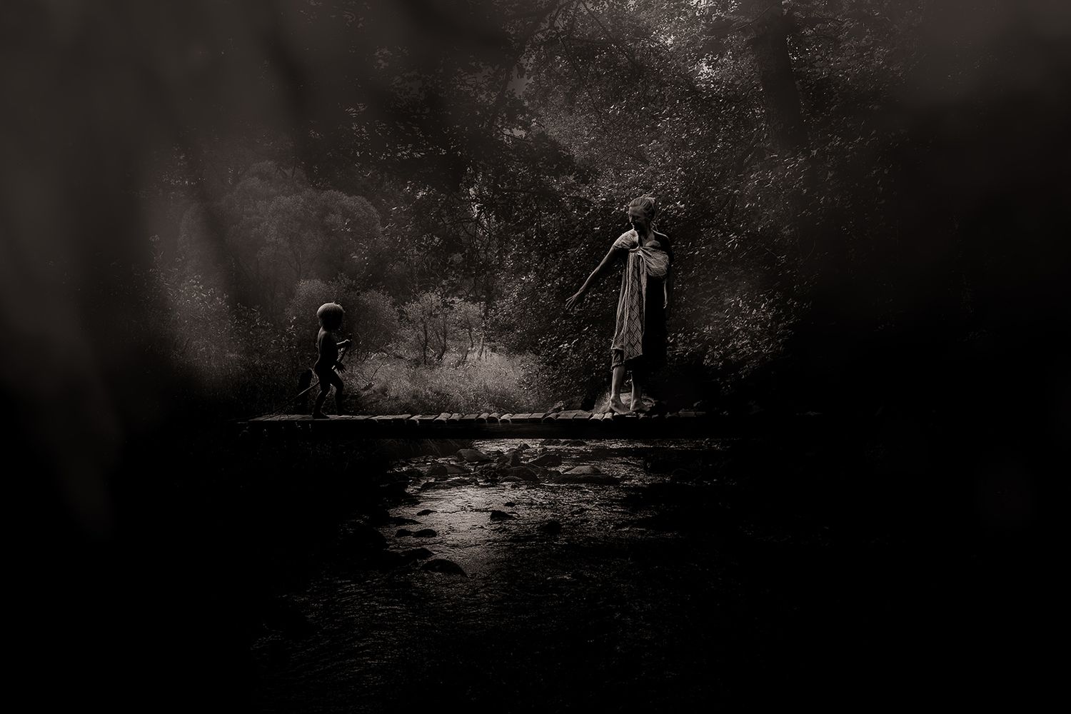 Dark moody photograph of two figures standing in a shadowy forest clearing with misty atmospheric lighting.