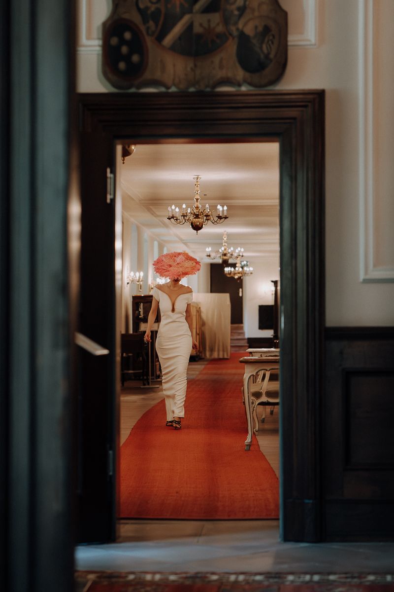 Eine sehr modische gekleidete Braut mit einem großen Hut von Marie Bernal läuft über eine langen Flur mit rotem Teppich im Schloss Vollrads.