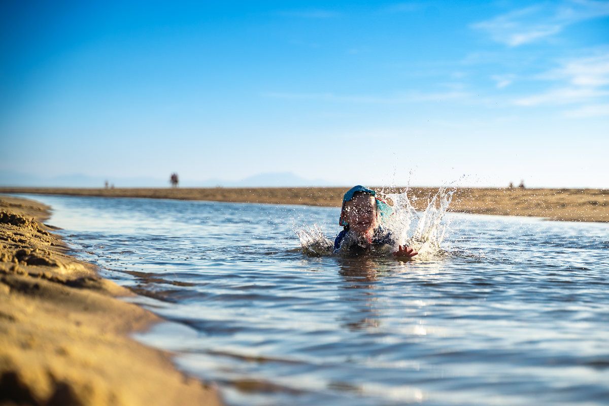 Person swimming in a shallow river on a sunny day with blue skies and sandy shores in the background.