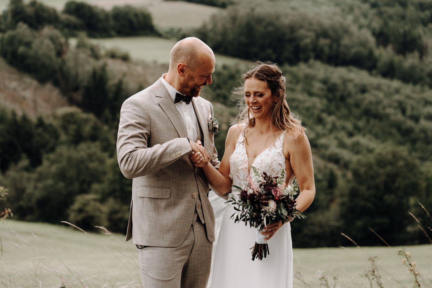 Bride and groom sharing a joyful moment outdoors, with lush green hills in the background on their wedding day.