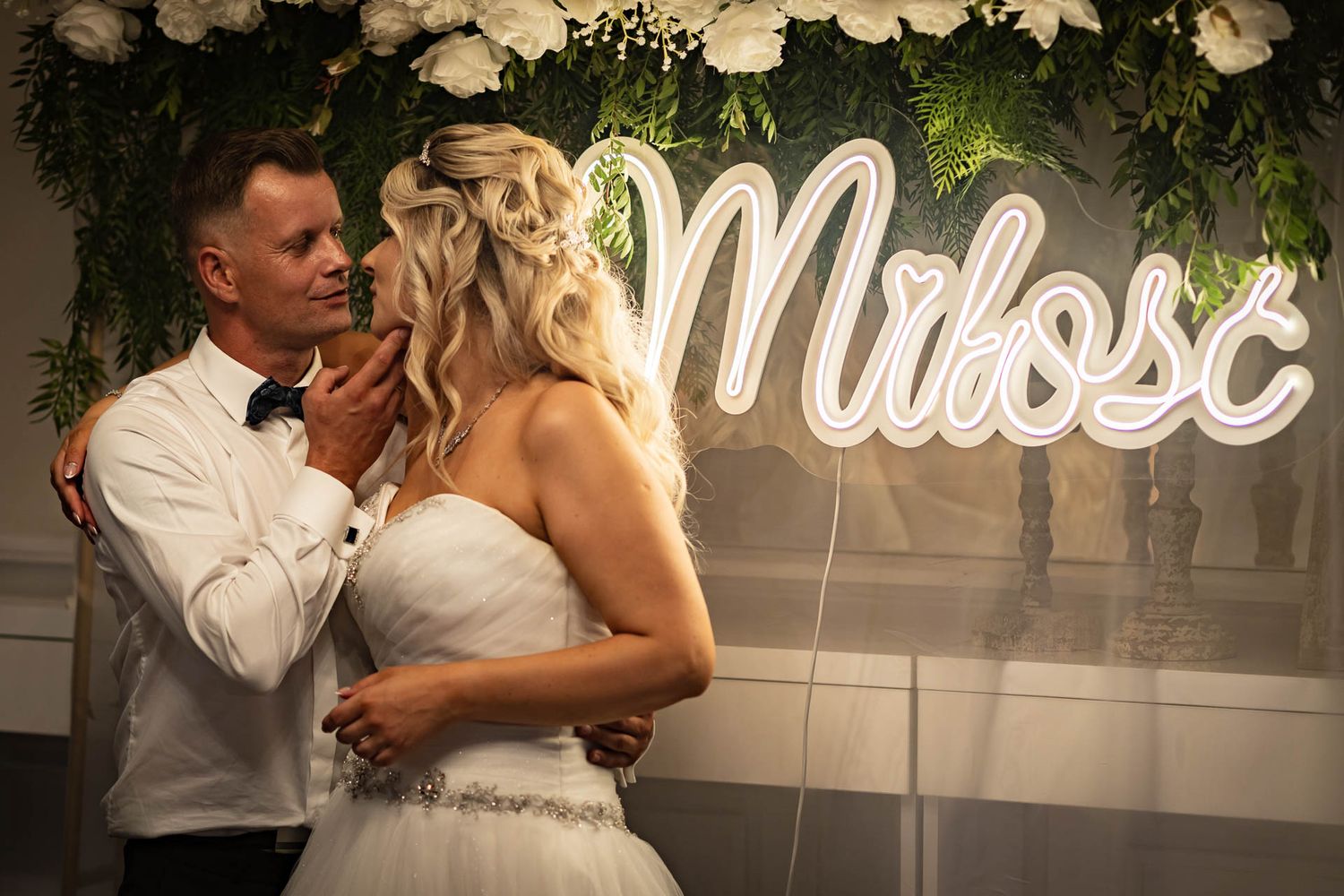 Wedding couple embraces under illuminated neon signage during their reception celebration.