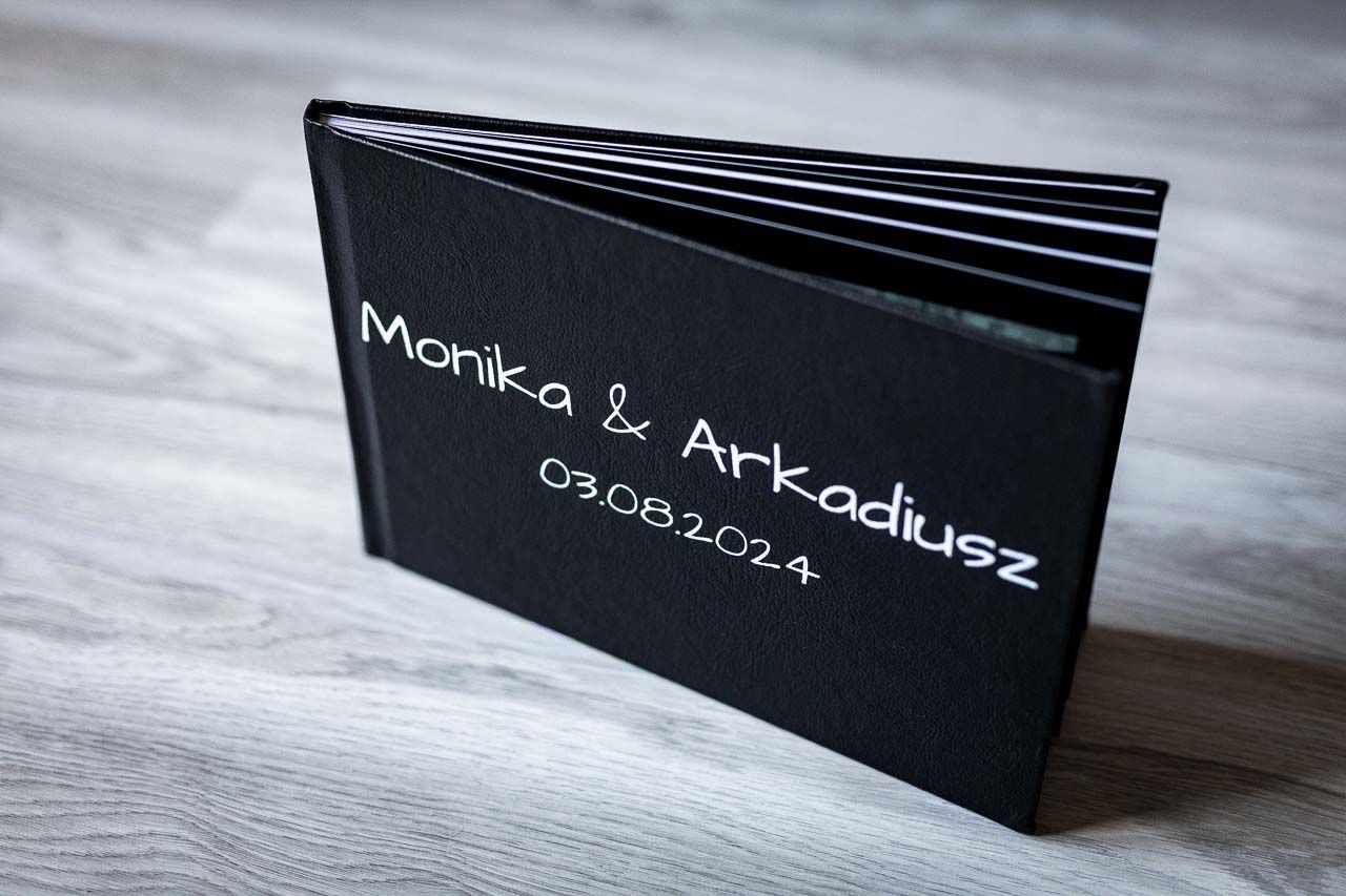 Professional black wedding photo album displayed on light wooden surface.
