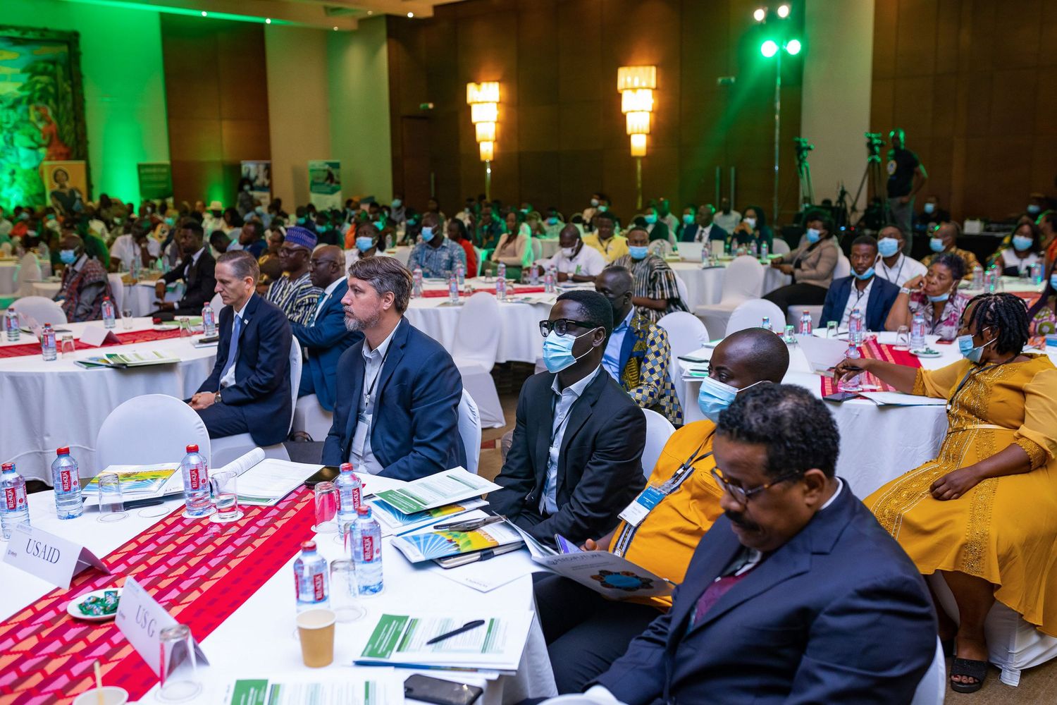 Conference attendees seated at round tables with red table runners during a professional event.
