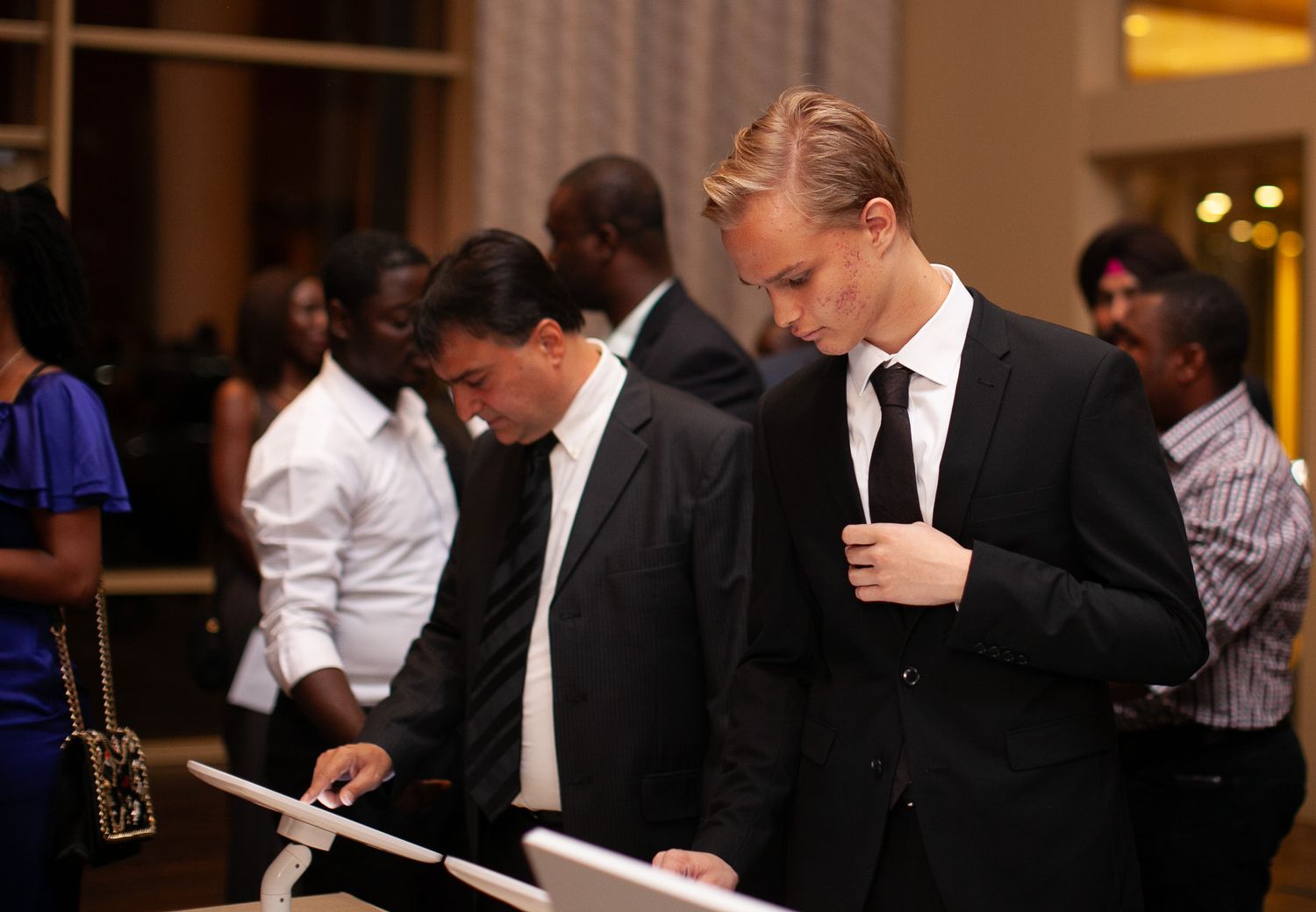 Business professionals in formal attire gather at a networking event while reviewing documents and having drinks.