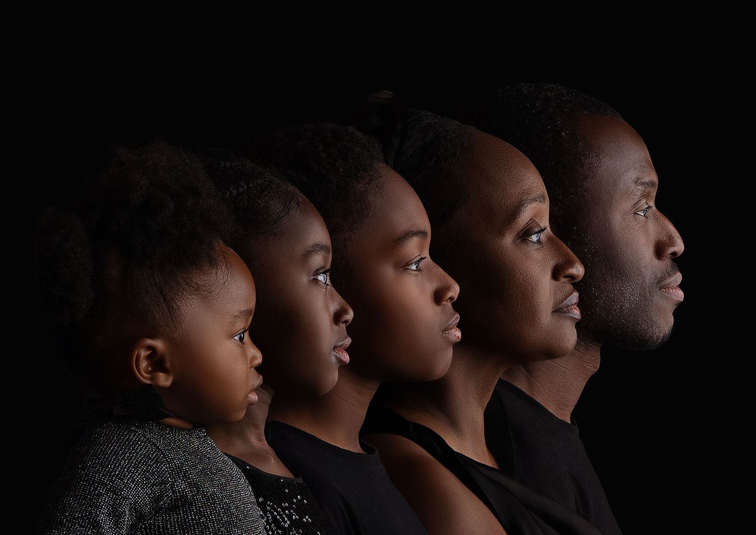 A series of silhouetted profiles against a dark background showing different ages and generations of people.