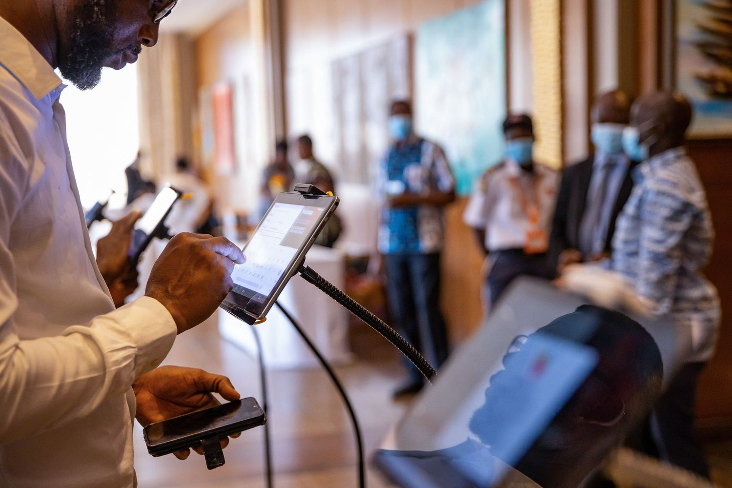 Person using mobile device in hallway with blurred group of people in background.