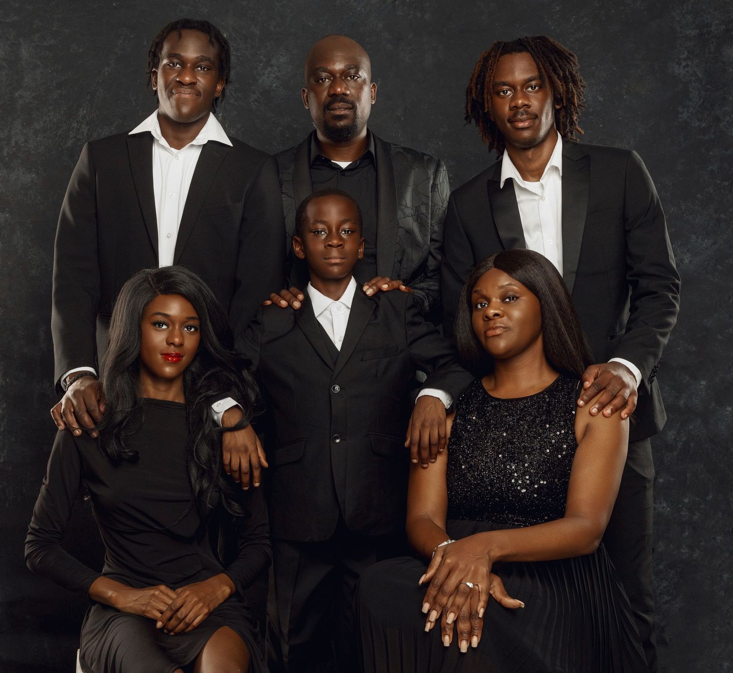 A stylish family portrait with multiple generations wearing coordinated black and white formal attire against a dark backdrop.
