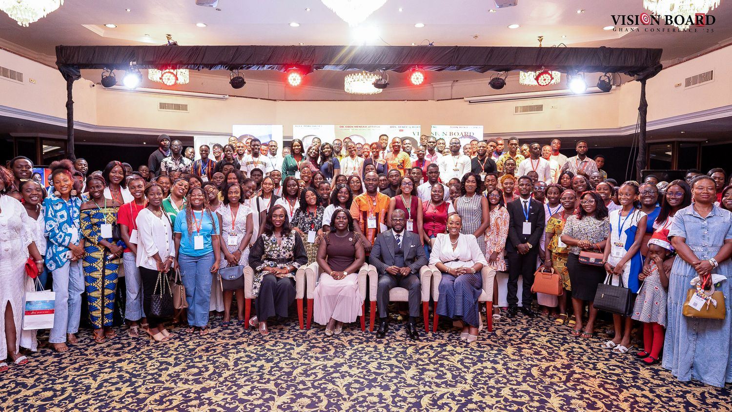 Large group photo of conference attendees gathered in a convention hall with stage lighting.