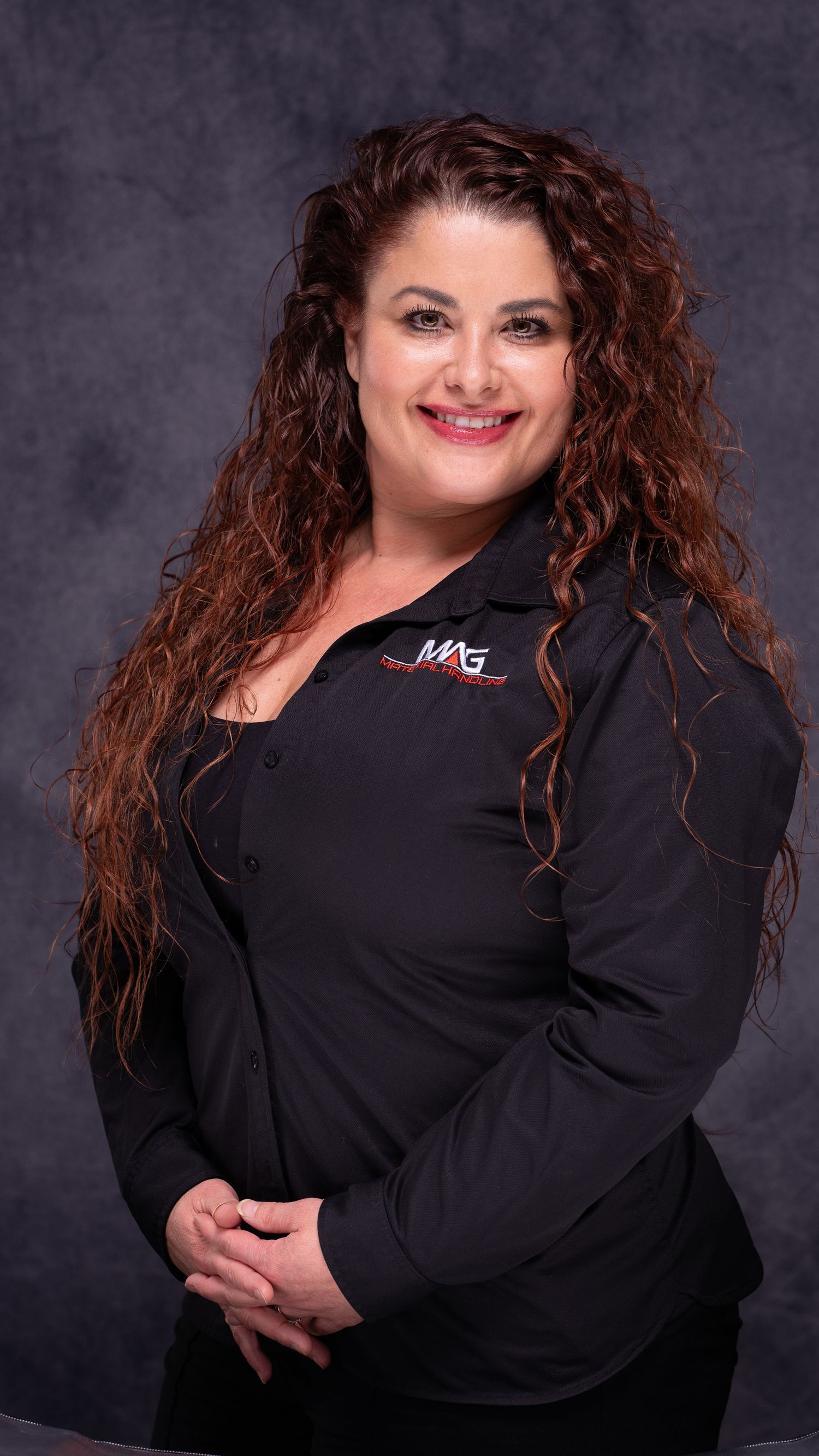 Woman in black jacket poses confidently for professional portraits against dark backdrop.