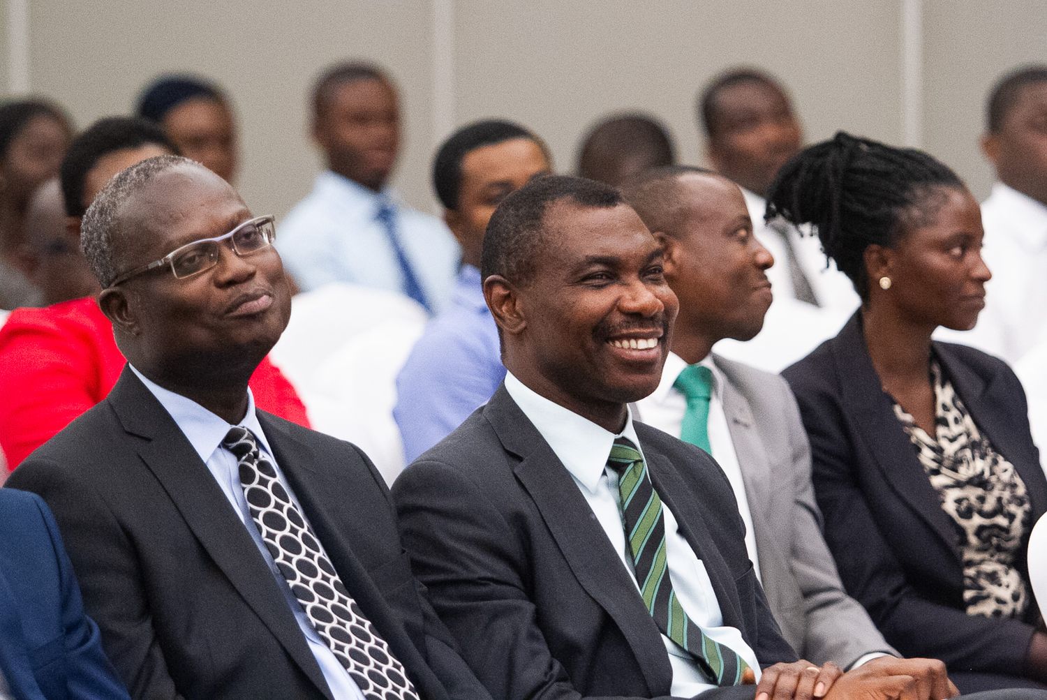 A group of people in formal business attire sit and smile during what appears to be a professional gathering or event.