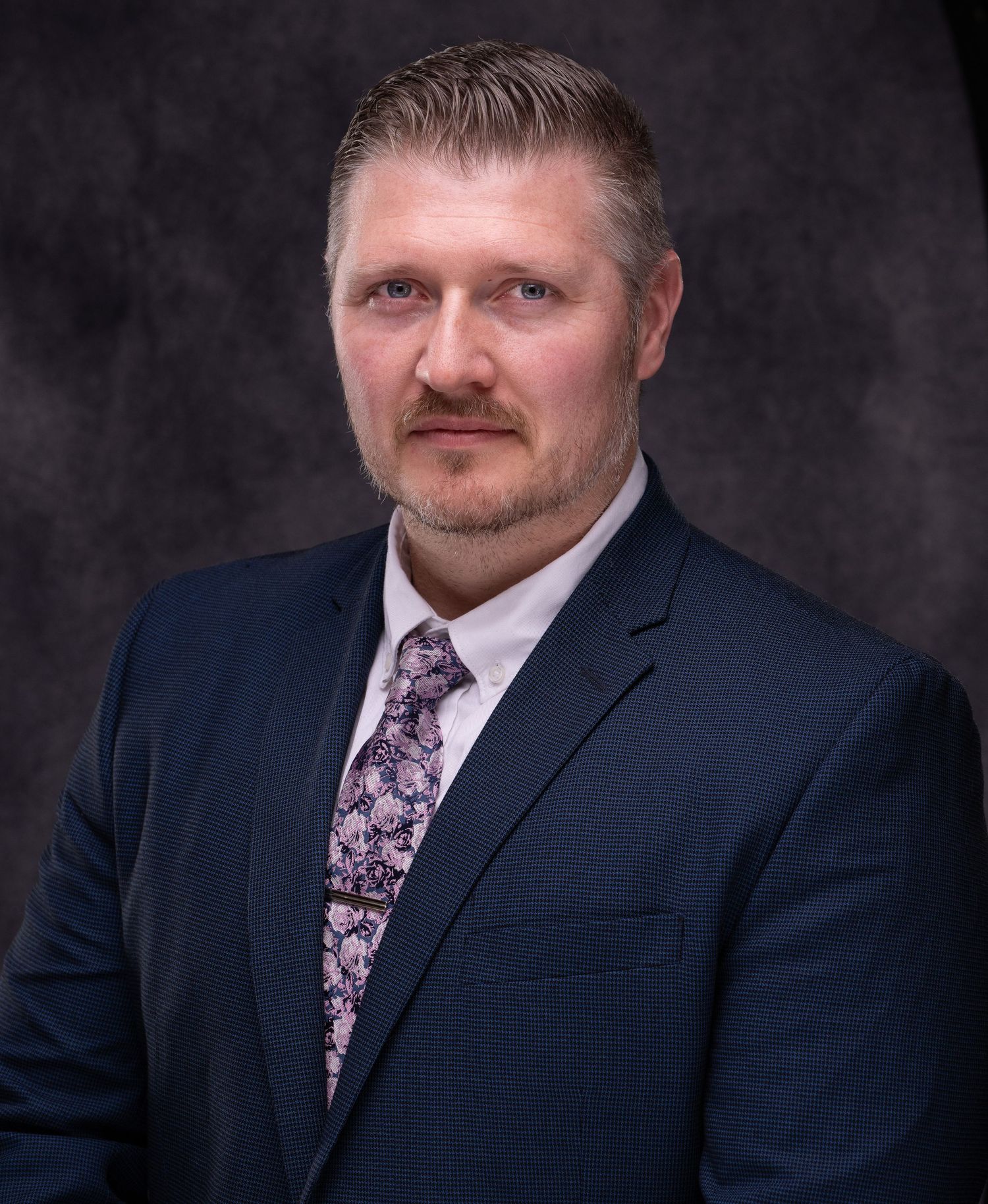 Professional headshot series of person in navy suit with floral tie against dark background.
