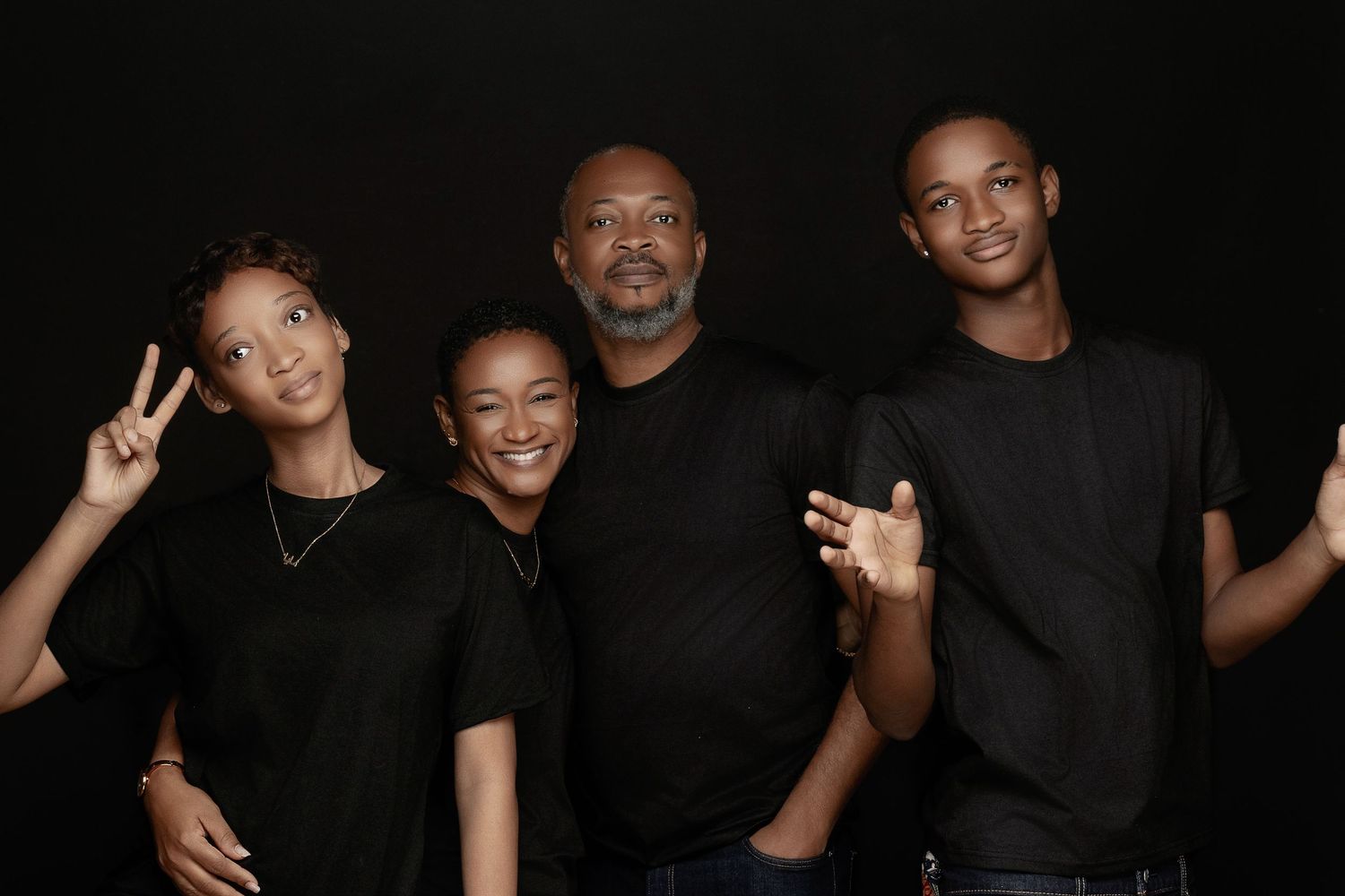 A group of people wearing black outfits pose together in a casual photoshoot setting against a dark background.