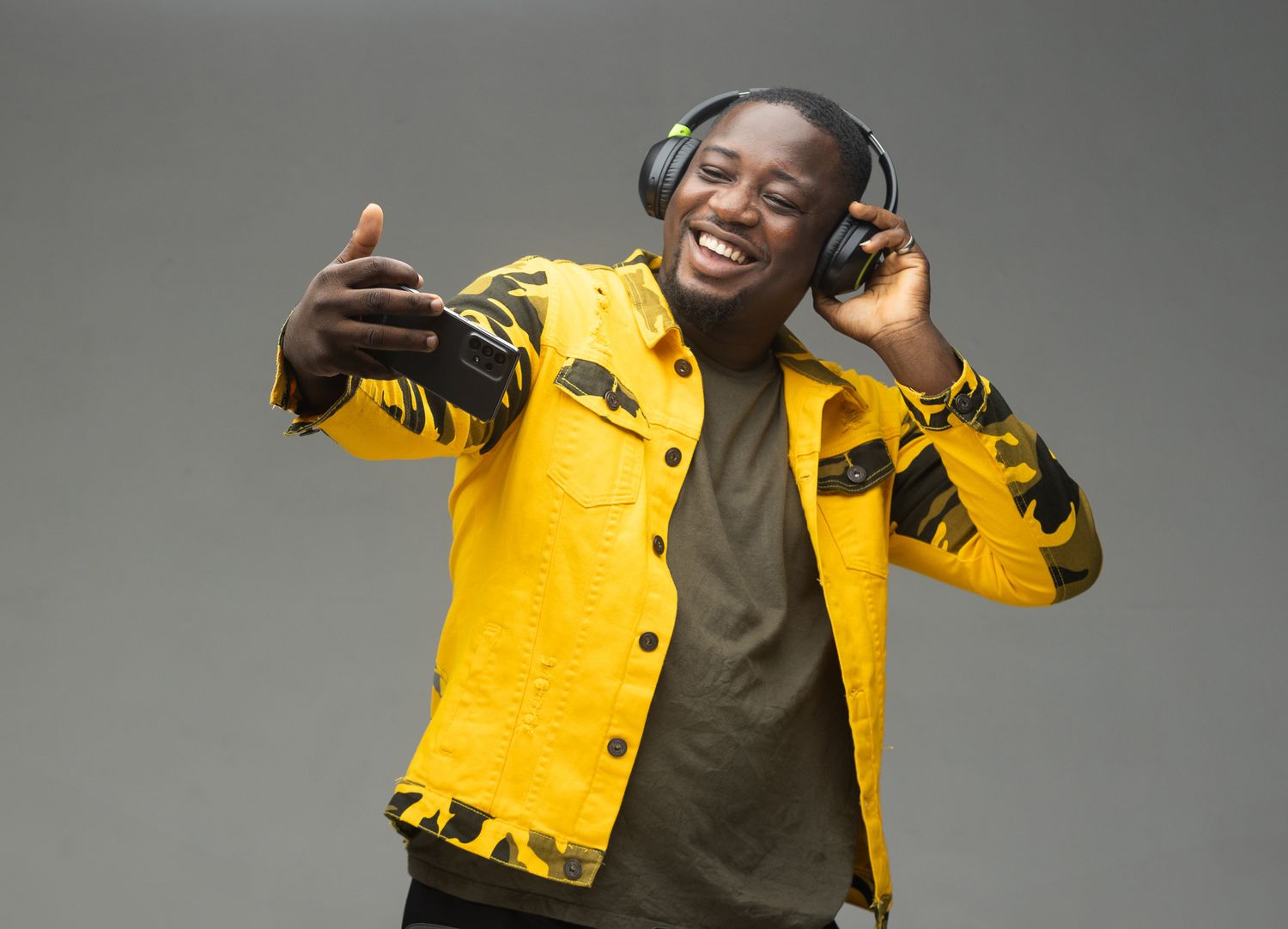A person wearing a bright yellow jacket dances and poses playfully against a gray background.