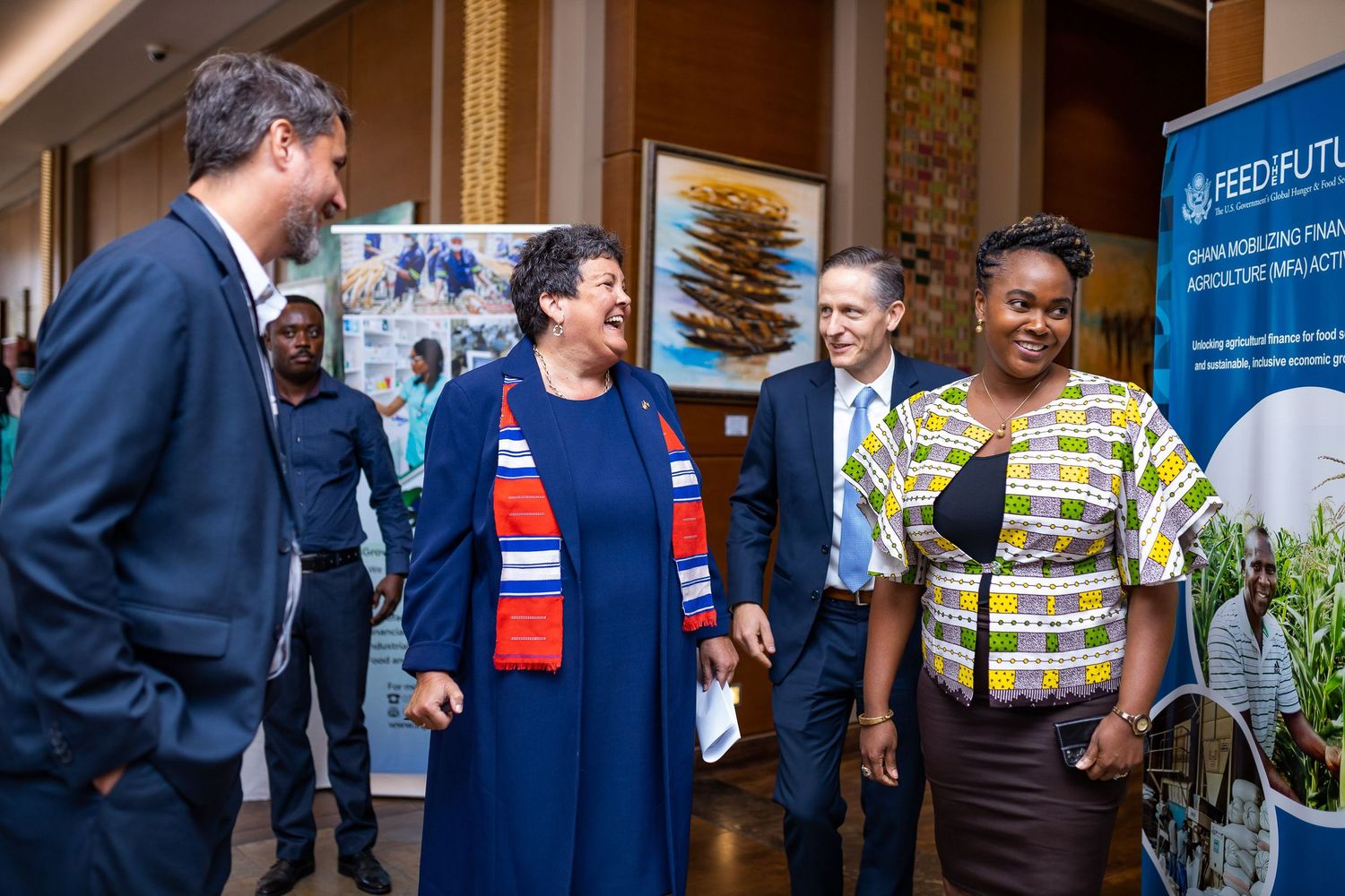 A group of people engaged in conversation at a professional event with banners visible in the background.