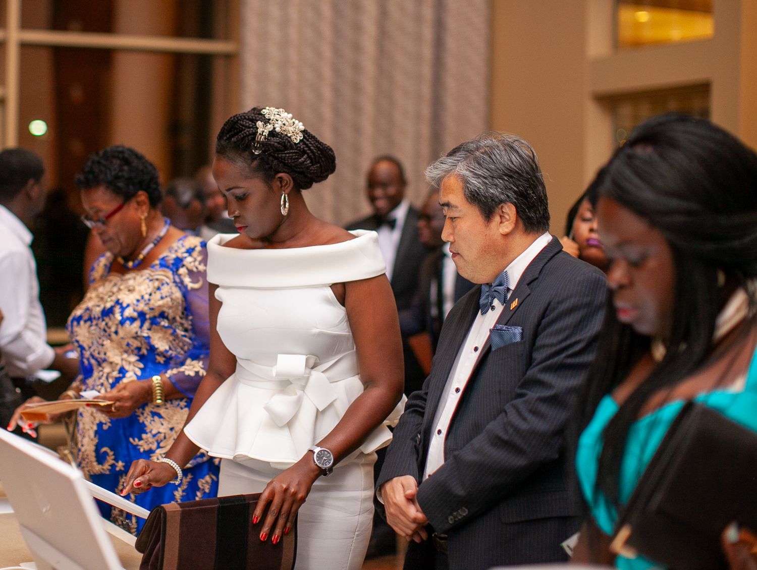 Event attendees in elegant attire reading programs while standing in a formal venue hallway.