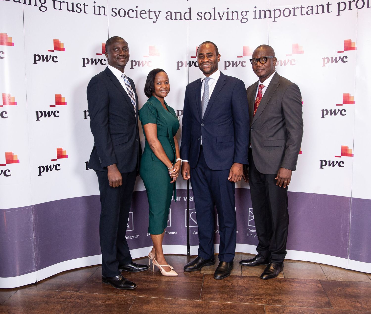 Business professionals in formal attire pose together at a PwC corporate event with branded backdrop.