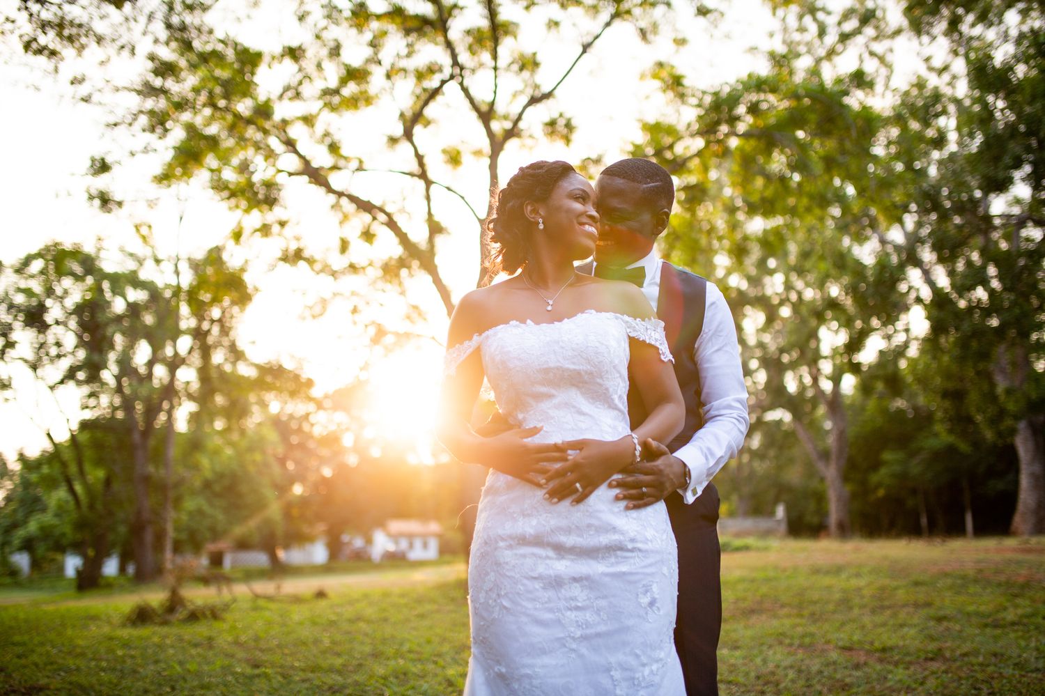 Couple in wedding attire embraces in a sun-drenched field during golden hour creating a romantic silhouette.