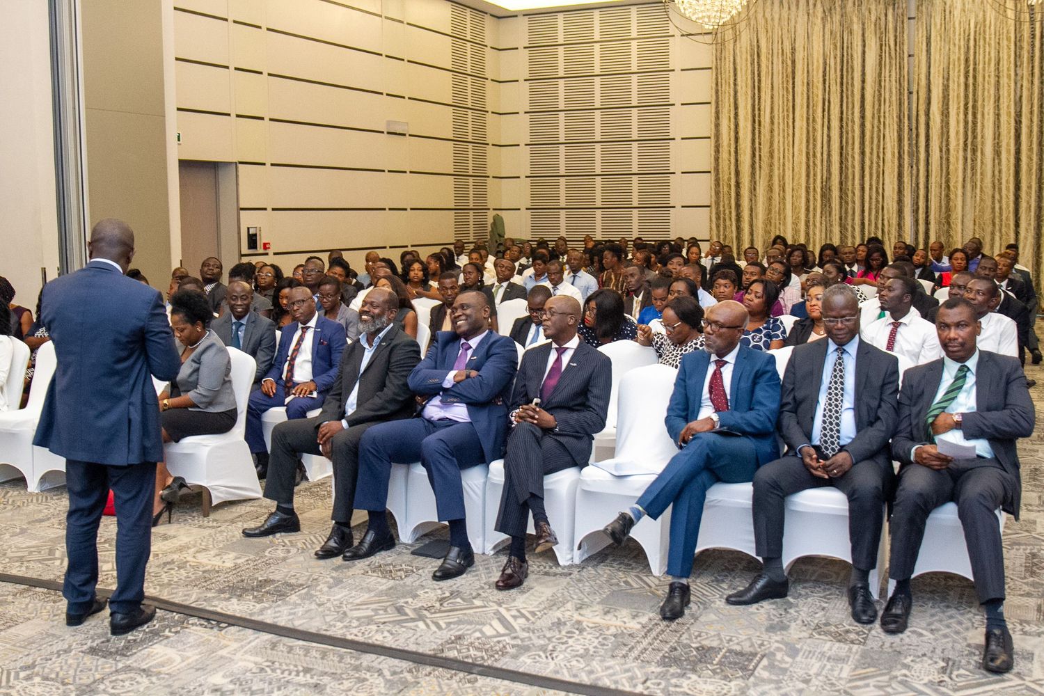 Business professionals sit in rows of chairs during a formal corporate conference or meeting event.