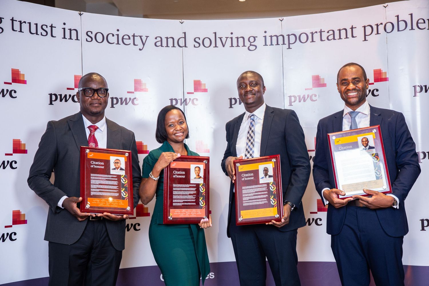 Four award recipients pose with red plaques at a corporate event in front of a branded backdrop.