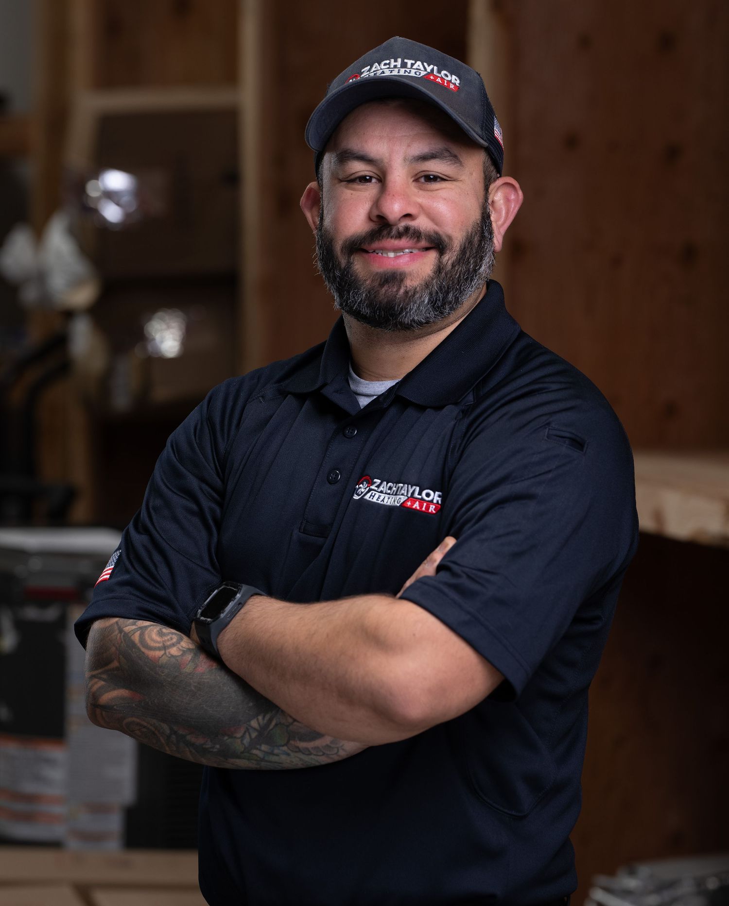 Professional in black uniform and baseball cap poses with crossed arms in dimly lit industrial setting.