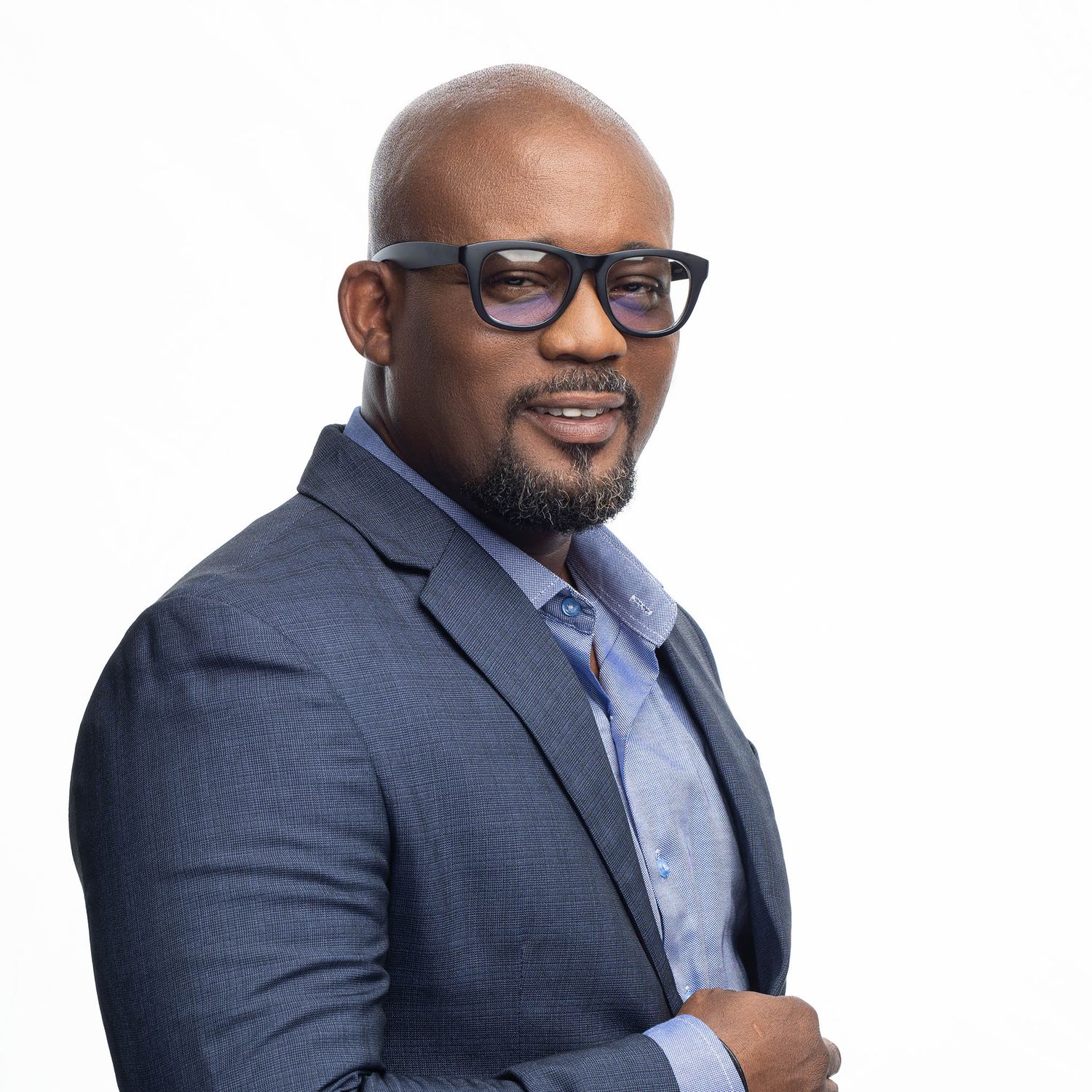 Businessman in blue suit and glasses smiles warmly in professional headshot series.