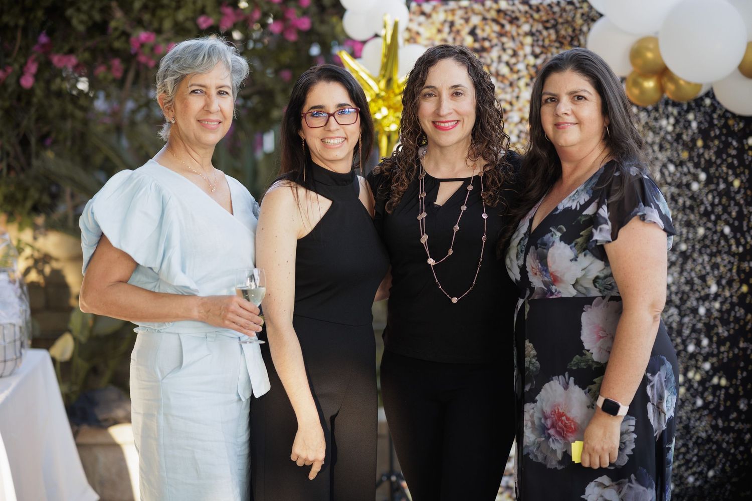 Friends posing together at festive party with balloons and floral decorations.