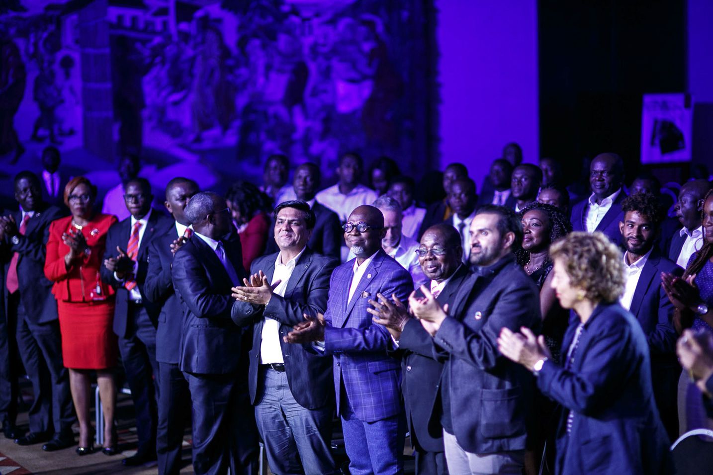 Crowd of attendees gathered at an event venue under dramatic purple lighting.