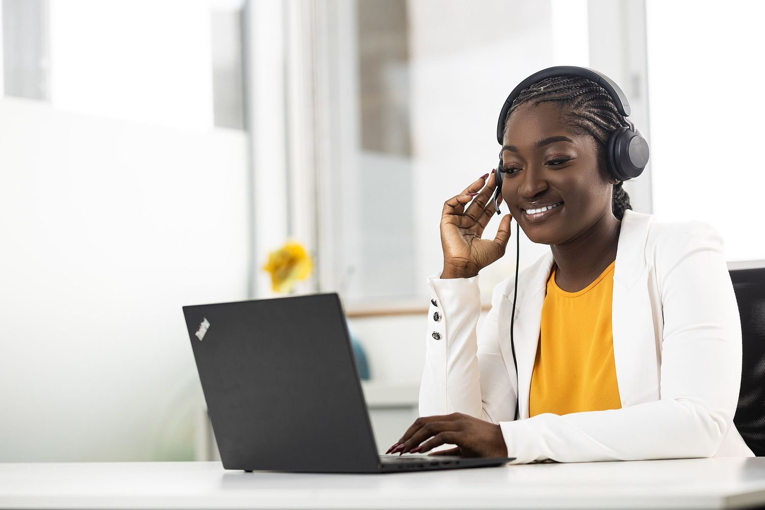 Professional working on laptop while wearing headphones in bright office setting.