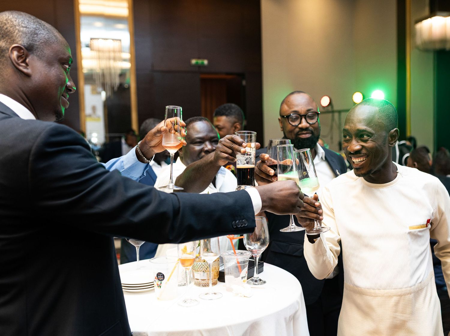 People raise their glasses in celebration at an indoor gathering with warm lighting and festive atmosphere.