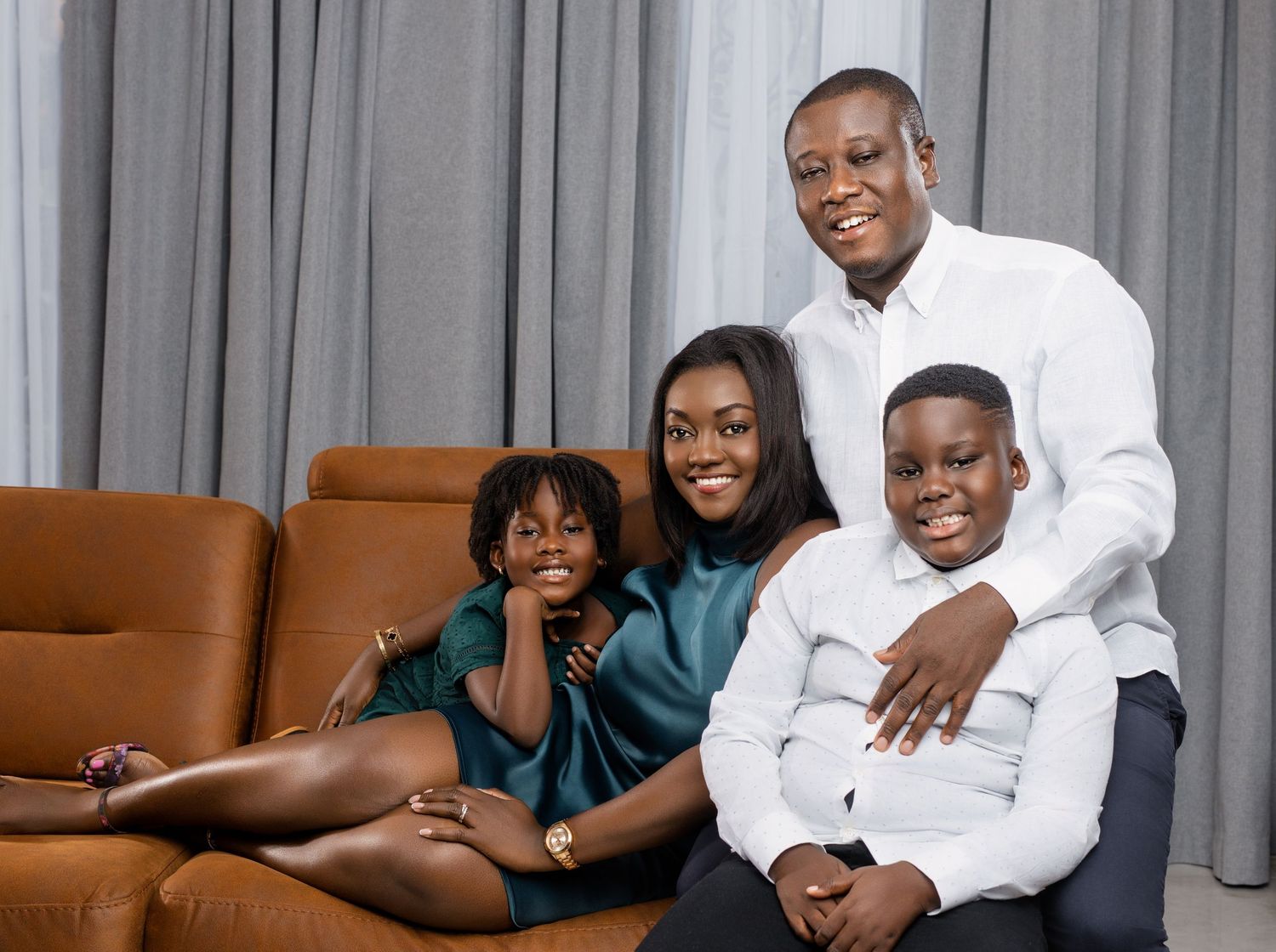 A family of four poses together on a brown leather couch wearing coordinated white and teal outfits.
