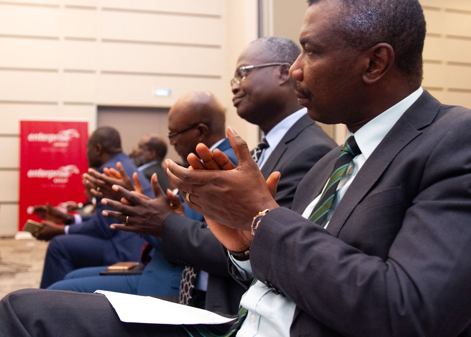 Business professionals in suits take notes during a corporate meeting or conference presentation.