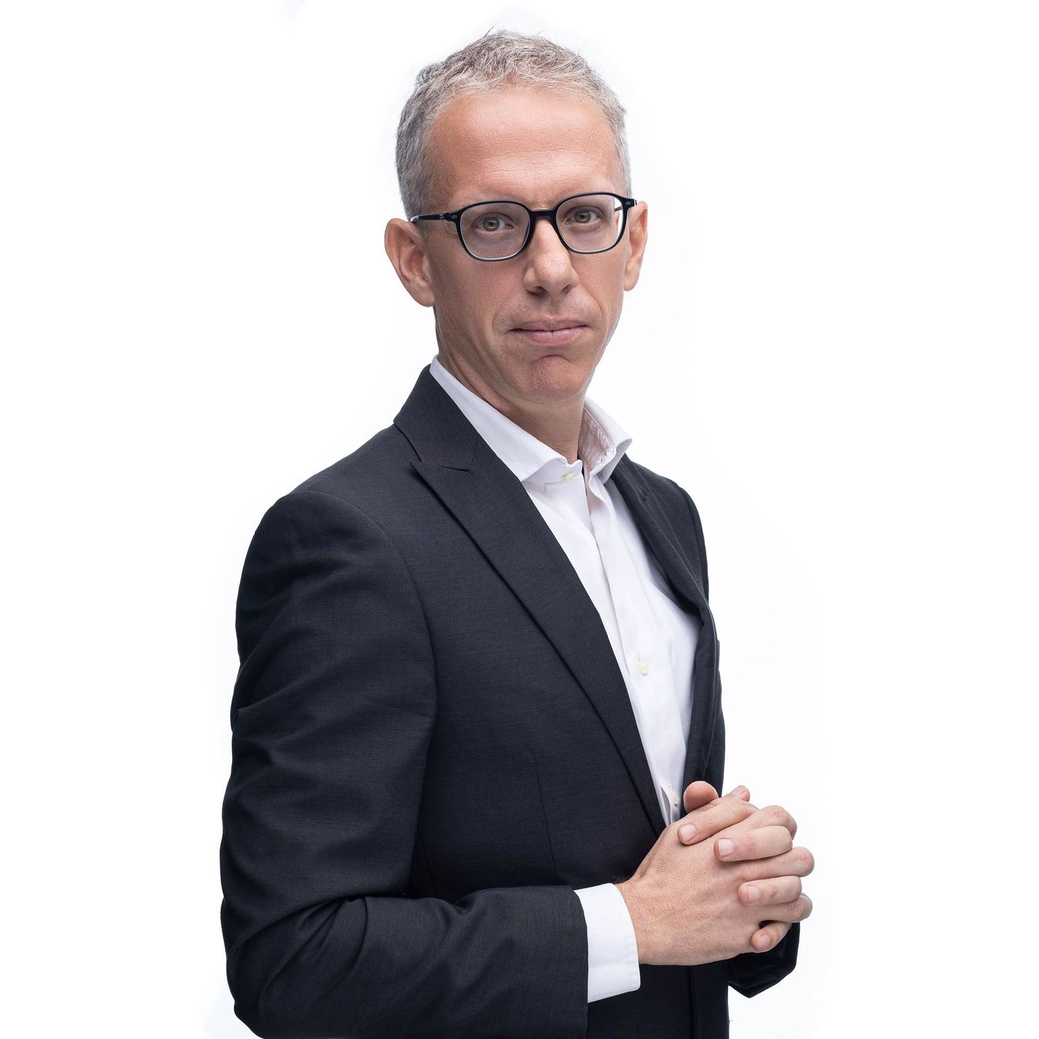 Professional businessman in black suit and glasses poses confidently against white background.