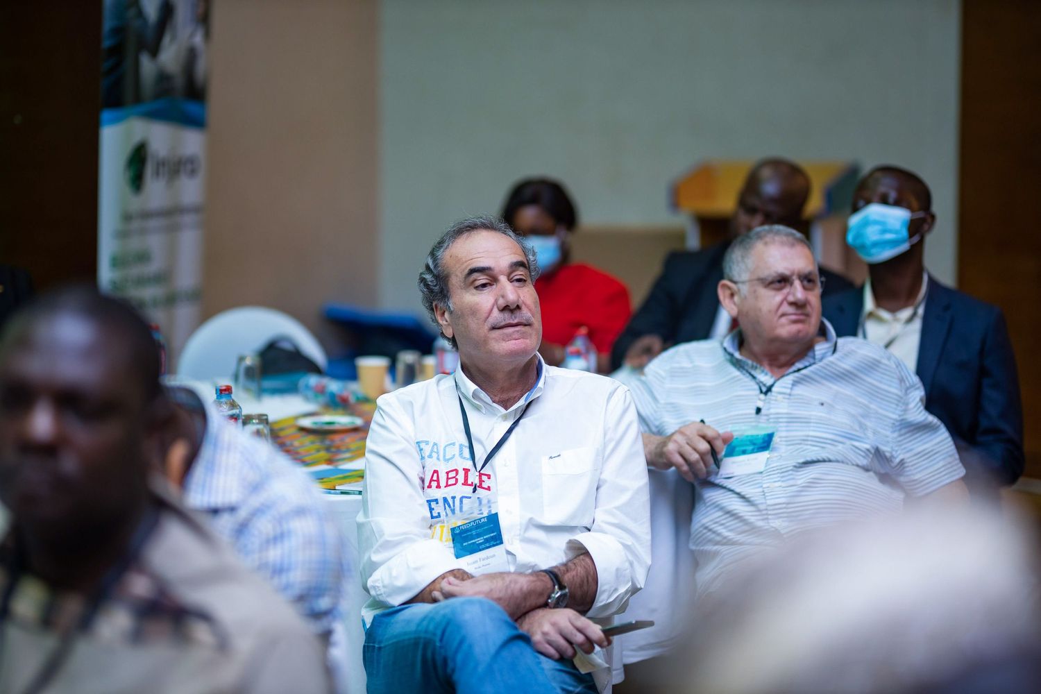 People wearing masks sit and listen attentively during a conference or meeting session.