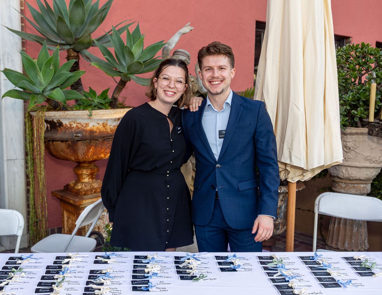Wedding guests find their table assignments displayed on escort cards at an outdoor reception with terracotta pots and succulents.