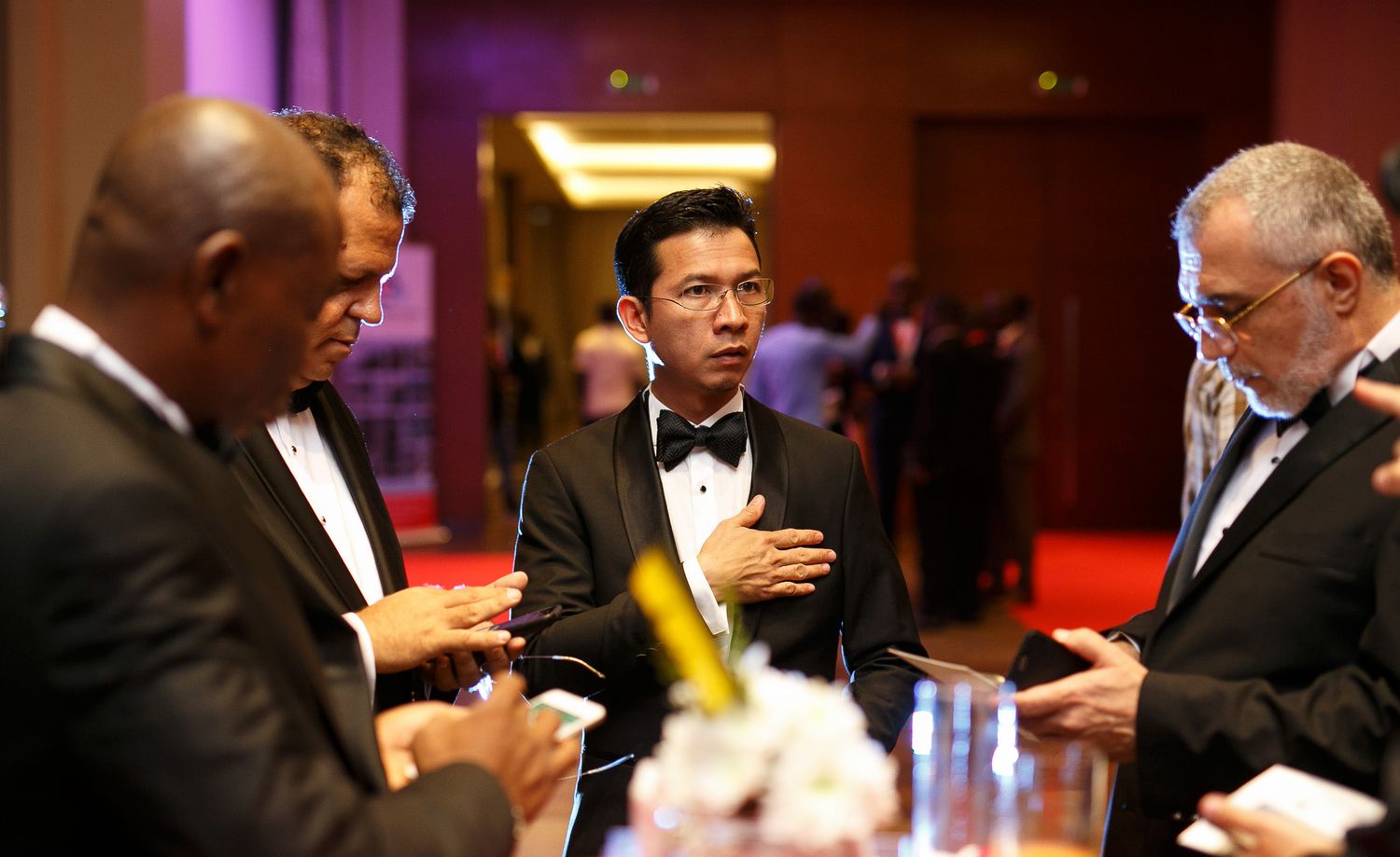 Group of formally dressed guests mingling at an evening reception with red ambient lighting.