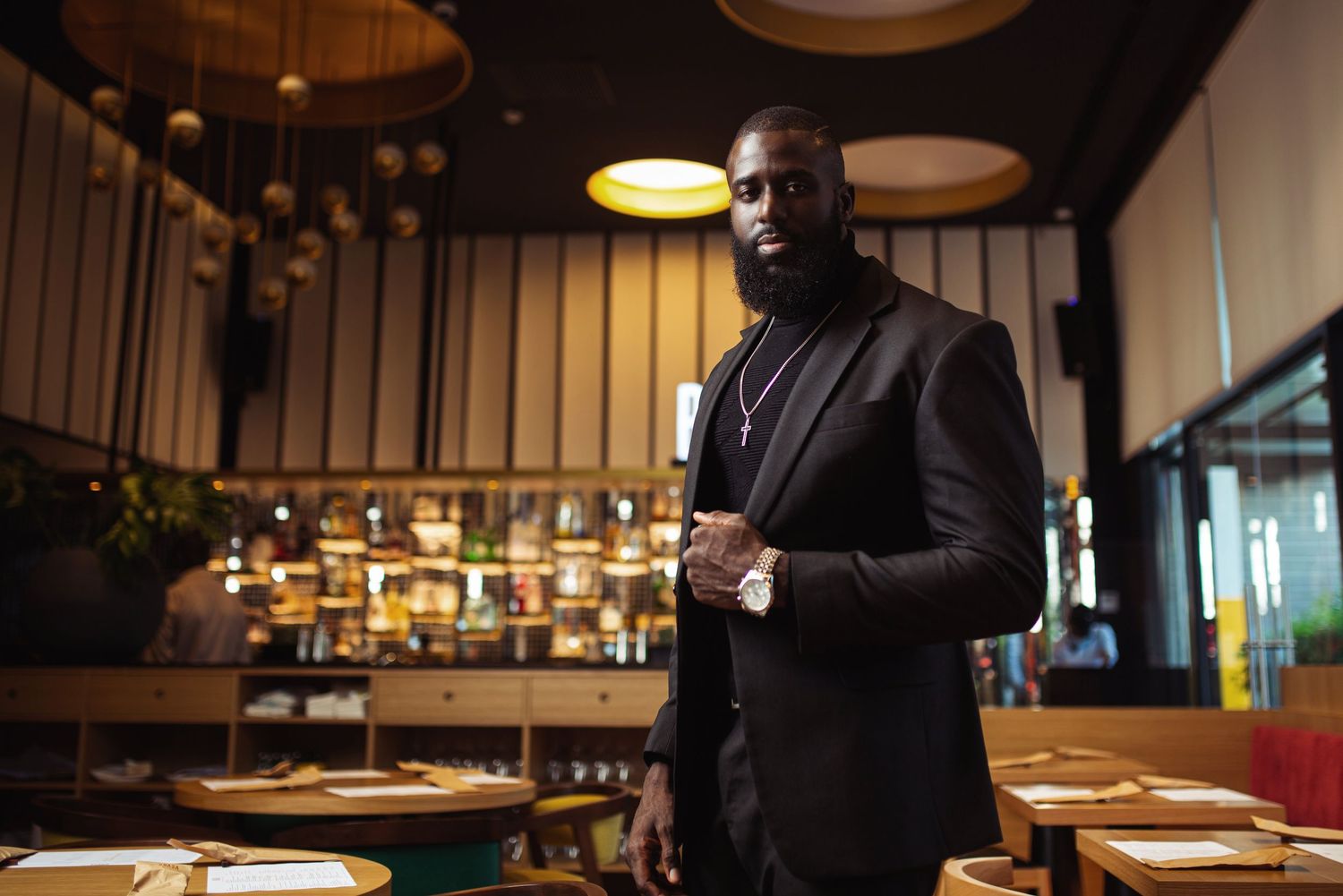 Business professional stands in modern restaurant setting with ambient lighting.