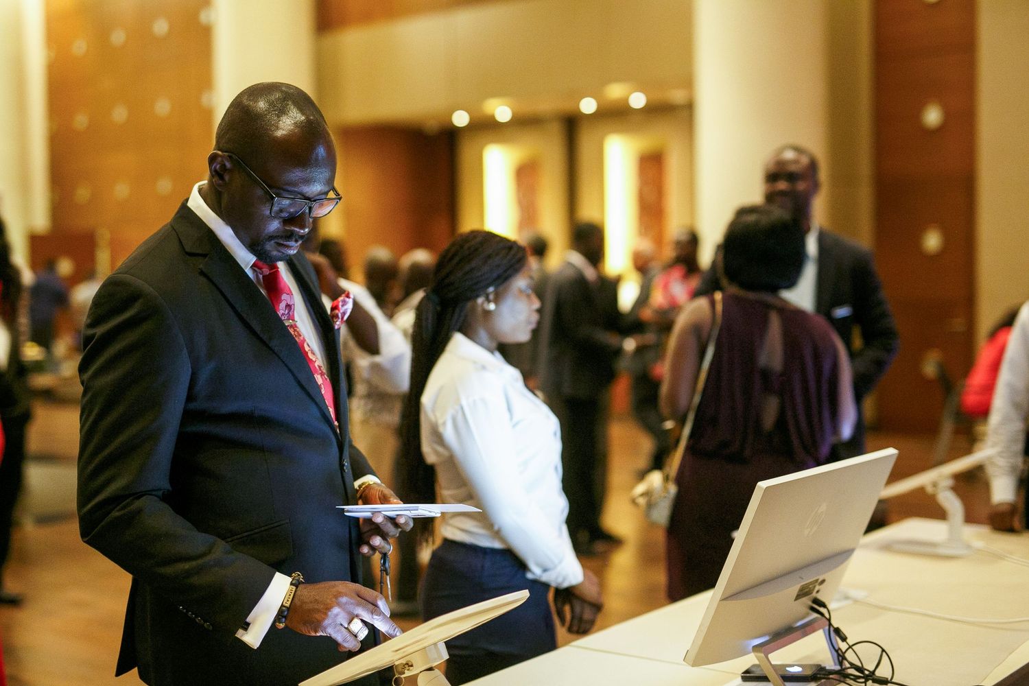 Business professionals work on laptops and take notes during a conference in a hotel meeting space.