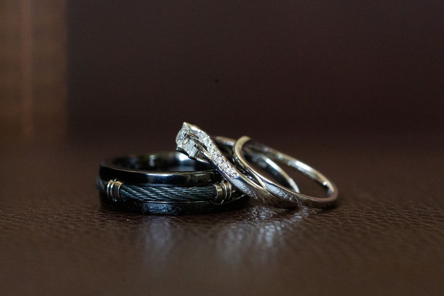 A close-up view of silver wedding rings with diamonds on a dark brown textured surface.