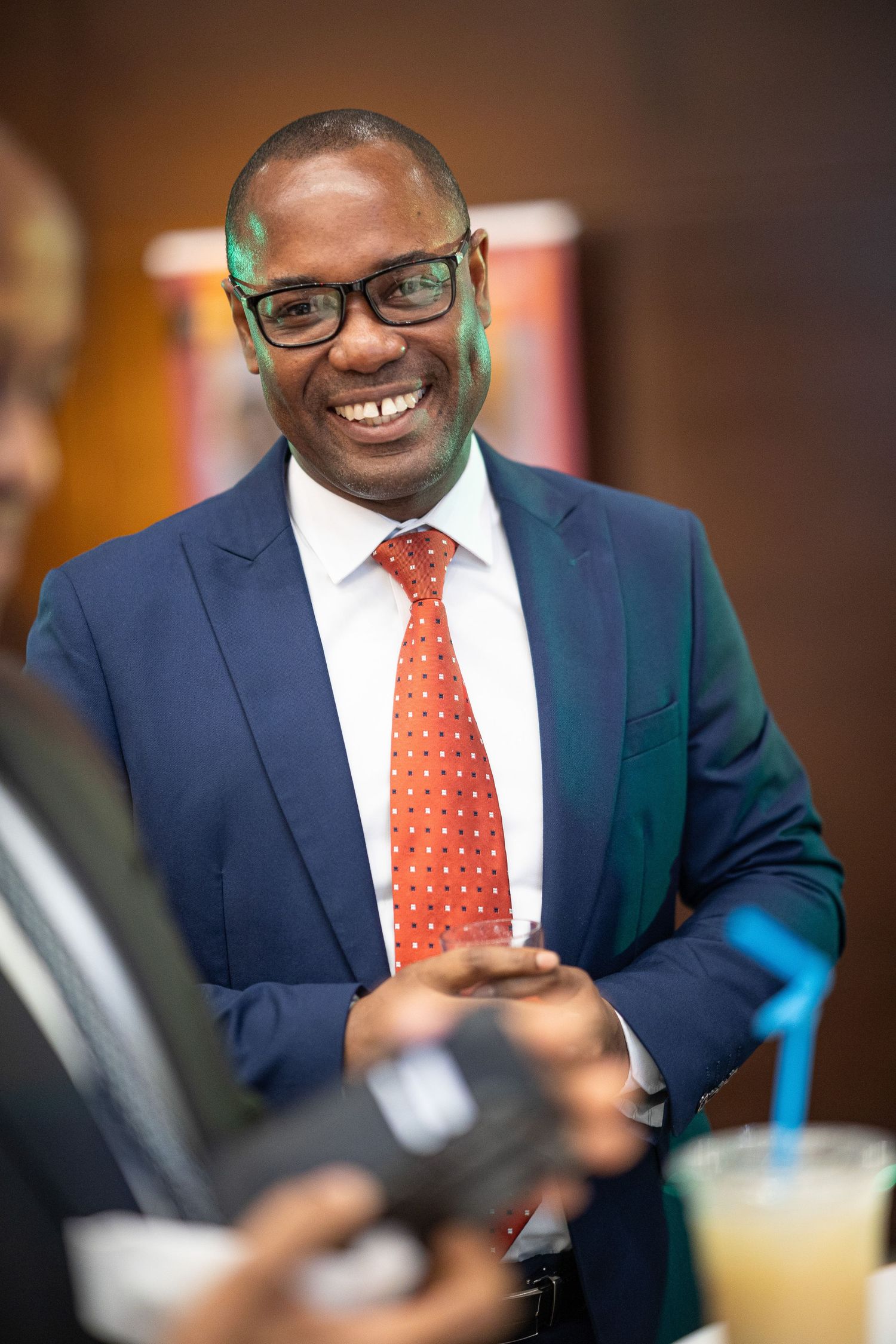 Professional wearing a navy suit and orange polka dot tie smiles warmly during a business meeting.